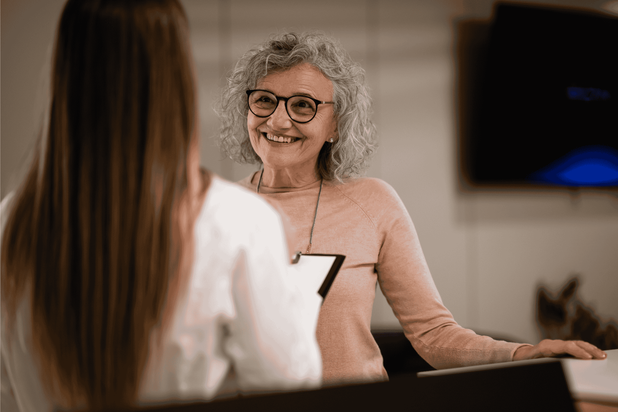 Friendly senior receptionist helping client, providing professional and welcoming support at an office front desk.