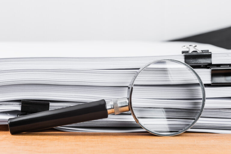 Close-up magnifying glass place on wooden table and search to edge of white documents.